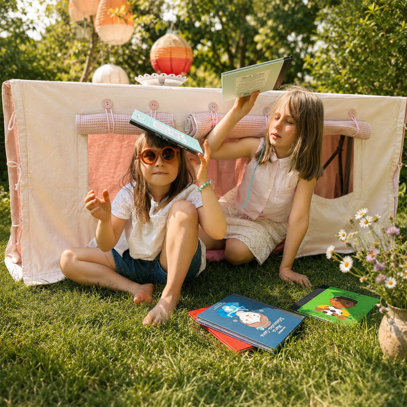 Kinder lesen und spielen vor einer Fundertable Spielwelt im Garten. Der Raum unter dem Tisch wird zum gemütlichen Ort für Geschichten, Fantasie und kleine Pausen mitten im Familienalltag.