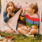 Zwei Kinder genießen eine Teeparty vor einem Fundertable Spielhaus im Garten. Die geöffnete Tür schafft einen geschützten Raum unter dem Tisch für Rollenspiele, gemeinsame Momente und fantasievolle Abenteuer im Familienalltag.