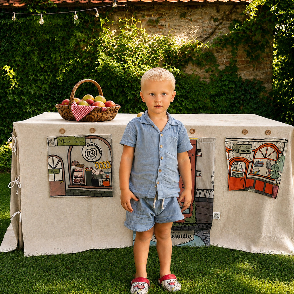 Fundertable Funderville mit Bäckerei- und Tierladen-Fenstern im Garten. Die textile Spielwelt unter dem Tisch schafft Raum für kreatives Rollenspiel, Fantasie und gemeinsame Familienmomente drinnen und draußen.