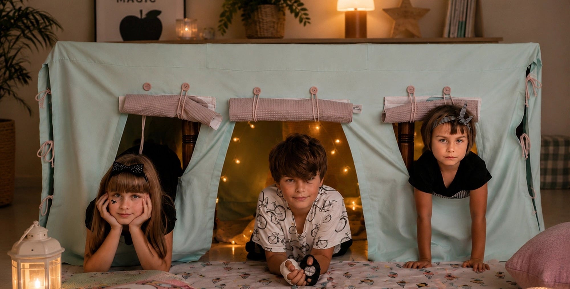 Drei Kinder spielen in einer mintgrünen Fundertable Base mit aufgerollten Fensterklappen und warmen Lichterketten im Inneren.